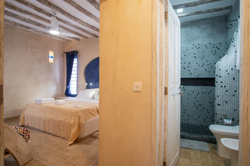 The bedroom opening onto the blue mosaic shower room